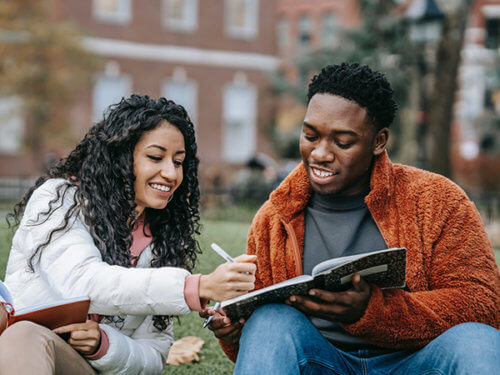 photo of two people of color on campus writing in composition books