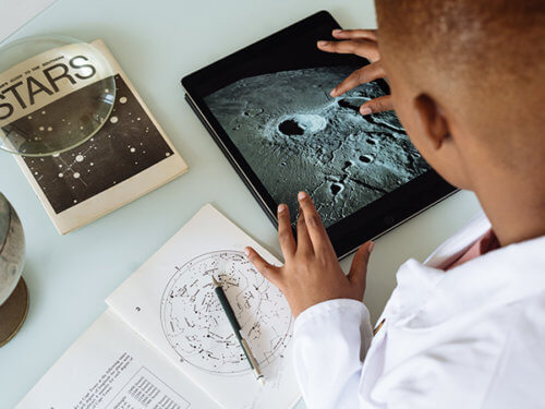 photo of a Black scientist in a lab coat studying moon craters on a tablet computer