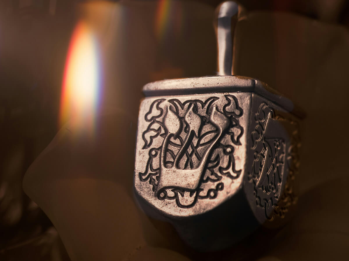 photo of a metal dreidel next to a candle flame